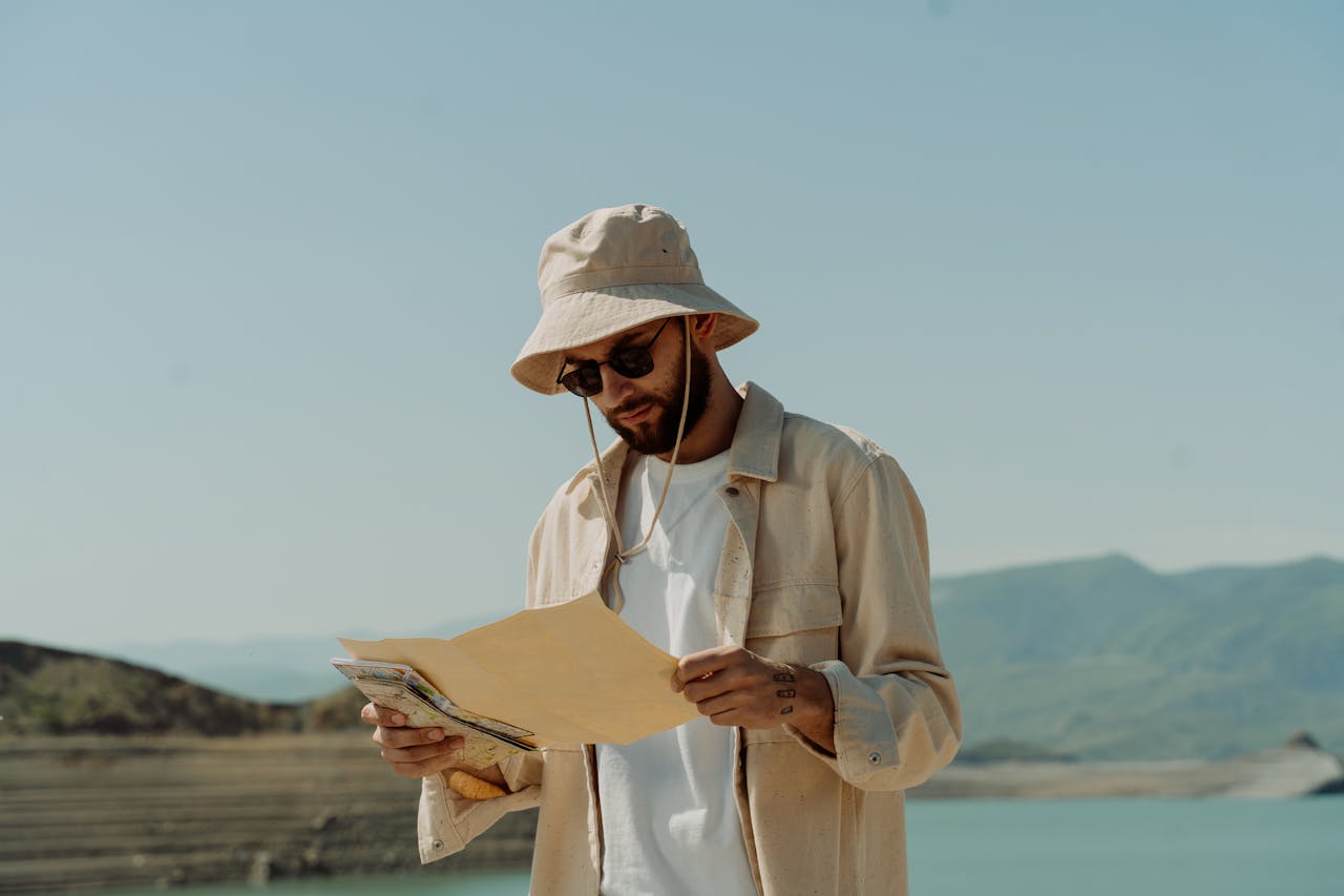 portfolio-05 Man in a bucket hat and sunglasses studies a map outdoors by a scenic lake.