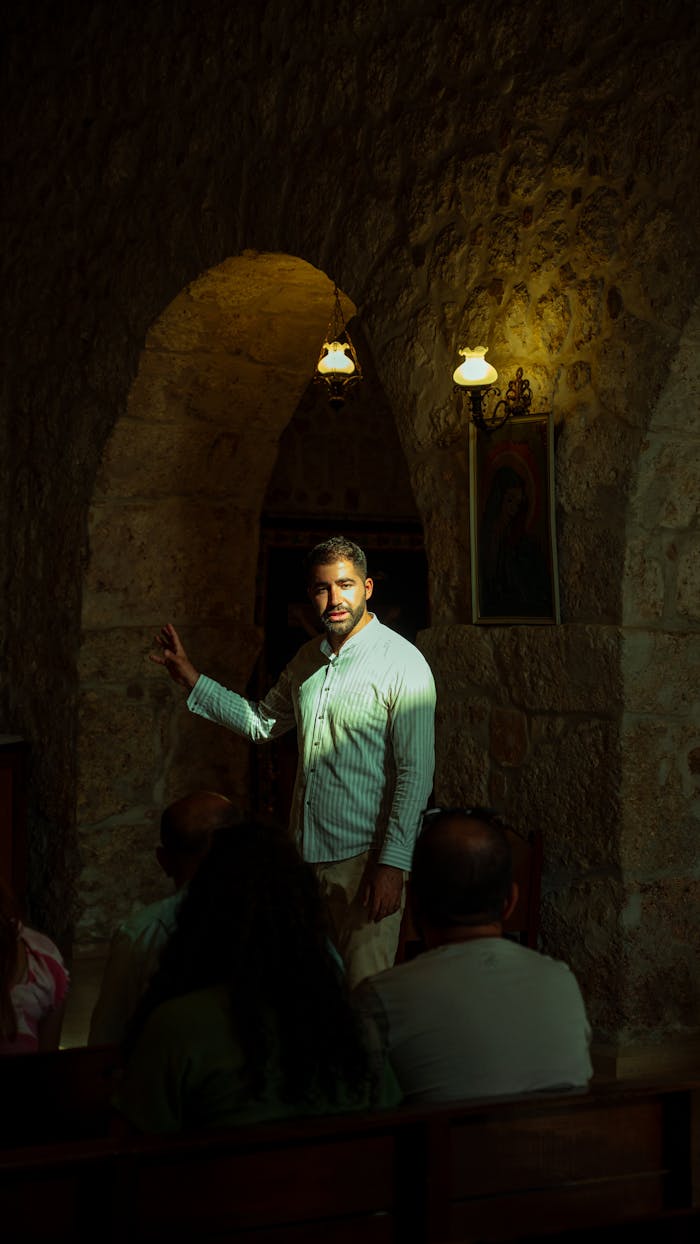 portfolio-01 A man speaks to a group in a stone-walled, arched historic building.